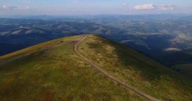 Dağın tepesinde, yemyeşil tepeler ve vadilerle çevrili dolambaçlı bir yolun hava görüntüsü..