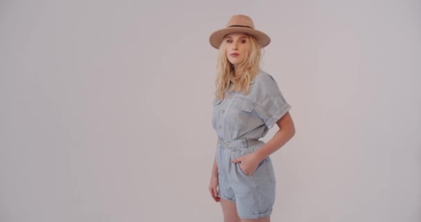 Une jeune femme portant une tenue décontractée en denim et un chapeau, posant avec confiance avec sa main sur le chapeau.