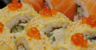 Somon yumurtası ve susam tohumlarıyla kaplı suşi rulolarının yakın plan görüntüsü, yanında taze somon dilimleri..