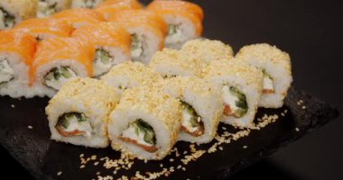 Siyah bir tepside somon, salatalık, krem peynir ve susam tohumlarıyla yakın plan suşi ruloları..