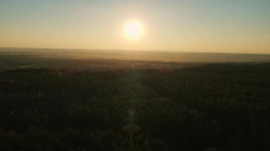 Güneş uçsuz bucaksız bir ormanın üzerinde yükselir, uzak mesafeden görülebilen sisli arazide altın bir ışık yayar..