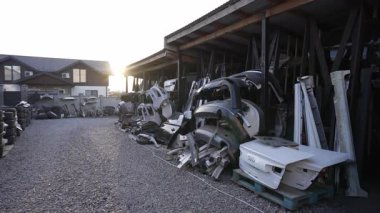 Kapılar, tamponlar ve lastikler de dahil olmak üzere bir yığın araba parçası arka planda bir bina bulunan bir çakıl deposunda depolanmıştır..