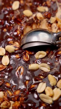 Parlak bir deseni, dağınık fıstıkları ve metal kepçesi olan zengin bir çikolatalı fıstık tatlısının yakın çekimi..
