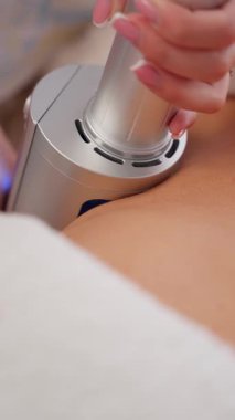 Bir el, bir klinikte mavi bir parıltı yayarak insan derisine uygulanan modern bir estetik cihaz tutuyor..