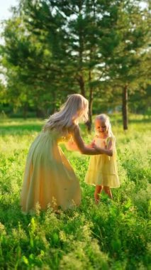 Sarı elbiseli bir anne ve kız yeşil çayırlarda güneşli bir anın tadını çıkarıyor, doğal olarak kaynaşıyorlar..