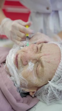 Kozmetik uzmanı yaşlı bir kadına yüz enjeksiyonu yapıyor. Güzellik kliniğine yakın plan estetik yaptırıyor..