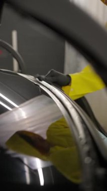 Sarı takım elbiseli bir işçi arabanın ön camını temizliyor. Profesyonel oto yıkama servisi sırasında detaylı olarak çekilmiş..