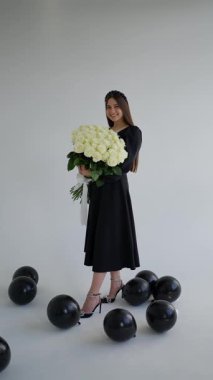 Etrafında siyah balonlar, ışıl ışıl gülümseyen bir kadın ve sarılmakta olduğu taze buket.