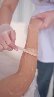 Kol kılı kesme tedavisini balmumuyla, güzellik uzmanının salonda spatulaya sürmesi. Güzellik stüdyosunda cilt bakımı, profesyonel el bakımı ile pürüzsüz cilt konsepti.