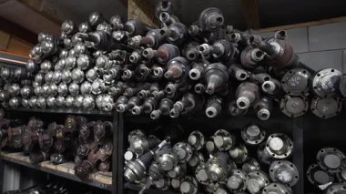 Depo raflarında kullanılmış otomotiv sürücü şaftları koleksiyonu, sıra sıra dizilmiş metal parçalar.