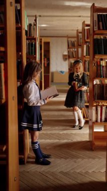 İki liseli kız kütüphanede kitap okuyor, sayfaları karıştırıyorlar..