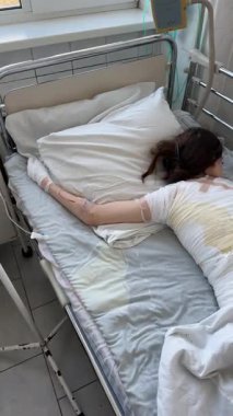 Tıbbi bandajlara sarılı olarak hastane yatağında yatan yaralı kız, steril klinik odasında ciddi yaralanan çocuk, doktor ve hemşirelerin bakımı altında tedavi görüyor..