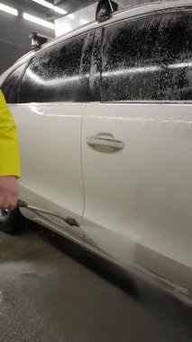 Yüksek basınçlı suyla yıkanan beyaz SUV 'nin yakın çekimi, kapalı mekan aydınlatma altında oto temizleme servisinde araba temizleme işlemi.