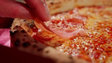Peynirli pizza, erimiş mozzarella ve domates sosunun üzerine ince bir dilim prosciutto koymak. İtalyan mutfağı sahnesi pizzanın son dokunuşunu çıtır çıtır çıtır yapıyor..
