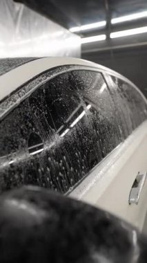 Araba yıkanıyor, sabun köpüğü ve su damlacıklarıyla kaplanıyor, siyah renkli camlara yansıyor..