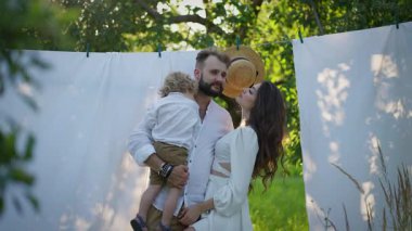 Beyaz elbiseli mutlu bir aile, bahçede bir yaz gününün tadını çıkarıyor. Güneş ve yeşillik doğada şefkatli bir sevgi ve bağlılık anı. Gün batımında..
