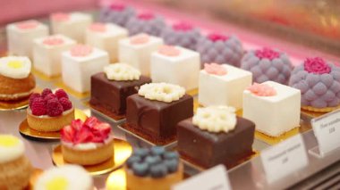 Çikolata kareleri, meyveli turtalar, kremalı kekler ve çiçeklerle süslenmiş pastalar da dahil olmak üzere cam vitrinlerdeki çeşitli enfes tatlılar..