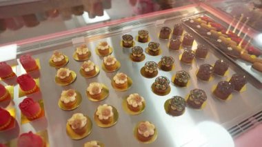 Şatafatlı hamur işleri sergisi için içinde gül şekilli krema tatlılar bulunan zarif bir cam vitrinde çeşitli mini pastalar ve pastalar..