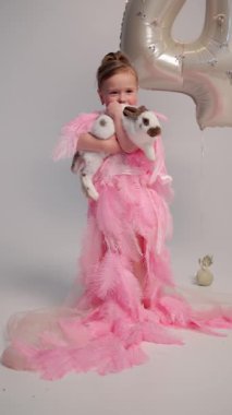 Küçük, tüylü, pembe tüylü bir kız. Elinde beyaz bir tavşan var. Gümüş balonla doğum gününde gülümsüyor..