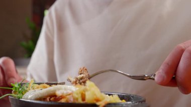 Bir insan masada otururken çatalla yemek alır..