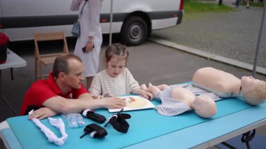 Bir adam, çocuğa acil müdahale teknikleri öğretirken mankenleri kullanarak kardiyopulmoner resüsitasyon öğretiyor..