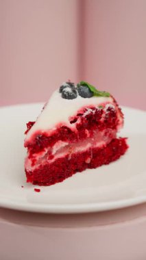 Kremalı ve yaban mersinli kırmızı kadife pasta, pembe arka planda beyaz tabakta servis edilir..