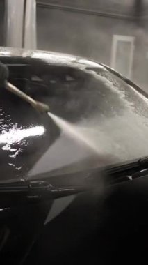 Profesyonel oto yıkamada yüksek basınçlı su jeti araba ön camını temizleme, detaylı yakın çekim görüntüsü.