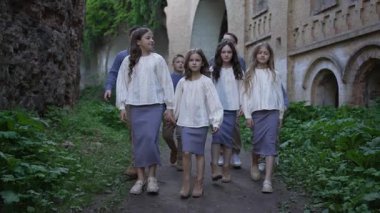 Antik kalenin yakınında geleneksel giysiler içinde yürüyen bir grup çocuk. Eski taş duvarları olan tarihi bir atmosfer..