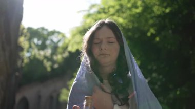 Teenage girl wearing a blue veil standing outside in the sun with a pensive expression.