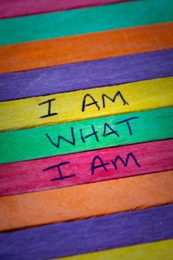 A hand written note representing gay pride stating I am what I am on a rainbow flag background in defiance of discrimination clipart