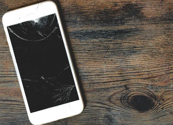 A close up of a damaged mobile phone with cracked screen for repair on a wooden background with copy space