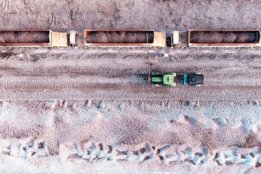 Aerial view directly above a mineral ore quarry with loaded railway wagons and a tractor with water bowser spraying water to dampen down airborne dust