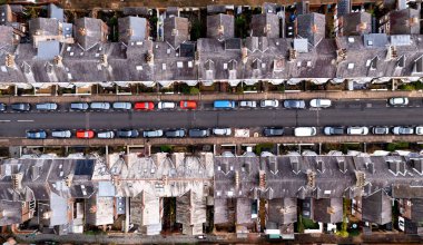 An aerial view directly above of the rooftops of back to back terraced houses on a straight suburban street with parked cars lining the road