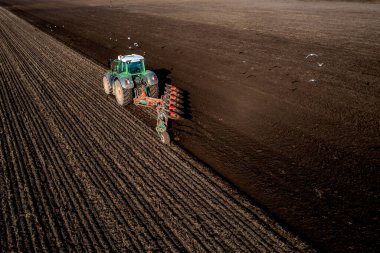 An aerial view of a tractor ploughing a fertile agricultural field with a flock of seagulls and birds scavenging for food in the soil