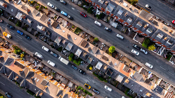 An aerial view directly above the rooftops of rows of back to back terraced houses with alleyways and gardens in a working class area of a Northern town in England