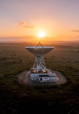 GOONHILLY SATELLITE EARTESİ, CORNWALL, UK - 2 Temmuz 2023. Gün batımında gökyüzüne bakan bir uydu anteninin havadan görüntüsü uzayın derinliklerinden iletişim gönderip alıyor.