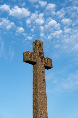 Düşük açılı bakış açısı, parlak mavi gökyüzünün altındaki antik bir taştan haça bakarak ölümü, umudu, ölümü ve kederi temsil eder.