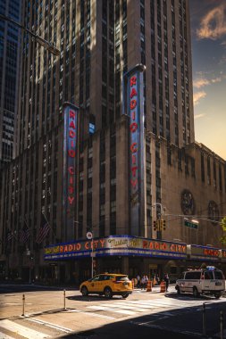 Radyo Şehri Müzikal Salonu, New York, ABD, 17 Eylül 2023. Günbatımında New York City 'de ünlü neon ışığı ve sarı taksiyle Radio City Music Hall' un girişinin dikey bir manzarası.
