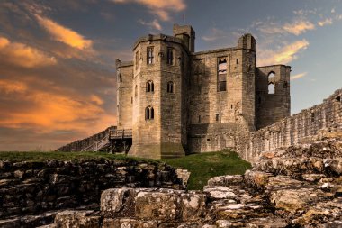 WARKWORTH CASTLE, NORTHUMBERLAND, UK - MARCH 16, 2024.  The fortified cross shaped Keep of Warkworth Castle and ruins with dramatic sky at sunset clipart