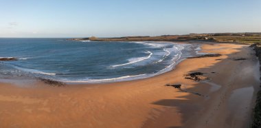 Aerial panorama landscape view of The England Coast Path along Embleton Bay beach and Dunstanburgh Castle at sunset clipart