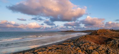 Aerial panorama landscape view of sand dunes and sandy beach at  Embleton Bay and Dunstanburgh Castle on the England Coast Path at sunset clipart