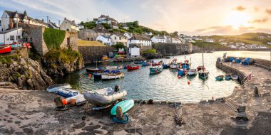 CORNWALL, UK 9 HAZİRAN 2024. Günbatımında Cornwall 'daki Coverack isimli tuhaf balıkçı köyünün gelgit limanına demirlemiş geleneksel Cornish balıkçı teknelerinin panoramik manzarası