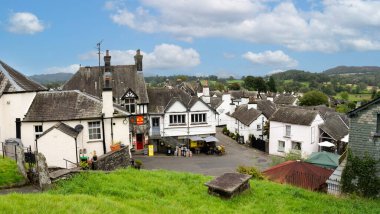 HAWKSHEAD, CUMBRIA, UK - SEPTEMBER 8, 2024.  Panoramic landscape of shops and tourist pubs and cafe in the centre of Hawkshead village in the English Lake District National Park clipart