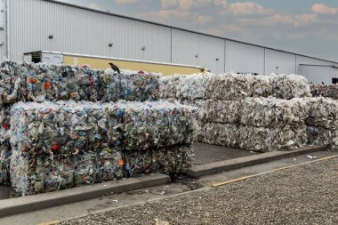 Kullanılmış plastik süt şişeleri ve kutular istiflenmiş balyalara doldurulmuş ve endüstriyel plastik atık geri dönüşüm tesisinde geri dönüşüme hazır.