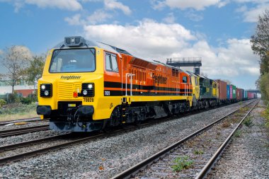 DERby, İngiltere - 5 Kasım 2024. Genessee ve Wyoming 'deki 70 sınıfı bir nakliye lokomotifinin demiryolu raylarında nakliye konteynırları taşıyan bir Intermodal tren taşıdığı profil görüntüsü.