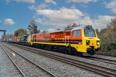 DERby, İngiltere - 5 Kasım 2024. Genessee ve Wyoming 'deki 70 sınıfı bir nakliye lokomotifinin demiryolu raylarında nakliye konteynırları taşıyan bir Intermodal tren taşıdığı profil görüntüsü.