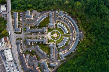 İngiltere 'de yeni inşa edilmiş banliyö evlerinin üzerinde dairesel bahçe tasarımı etrafında kıvrımlı mimari merkezli ve yeşil kuşak bölgesindeki odunları tahrip eden havadan tepeden aşağıya bir manzara.