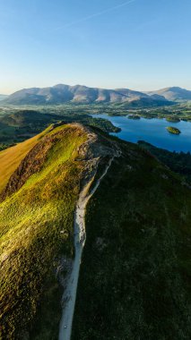 Derwent Water Gölü ve Keswick kasabası güneşli bir günde Kuzey Şelaleleri 'nin aşağısında bulunan İngiliz Lake District Ulusal Parkı' ndaki Catbell Dağı tepesi boyunca yürüme yolunun dikey manzarası.
