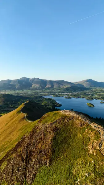 Derwent Water Gölü ve Keswick kasabası güneşli bir günde Kuzey Şelaleleri 'nin aşağısında bulunan İngiliz Lake District Ulusal Parkı' ndaki Catbell Dağı tepesi boyunca yürüme yolunun dikey manzarası.