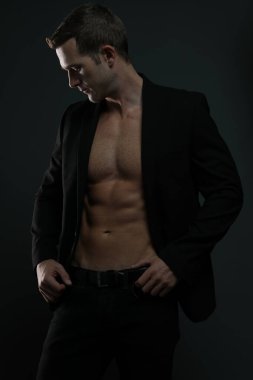 Ceketi açık tişörtsüz adam karın kaslarını gösteriyor.